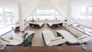 A modern spa room with reclining chairs, large windows, and potted plants. - Gartenhotel & Weingut Pfeffel Dürnstein (Durnstein)