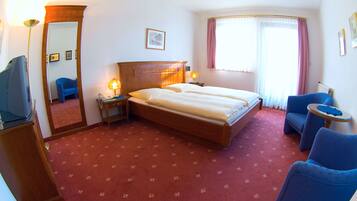 A hotel room with a bed, two bedside tables, a desk with a computer, a chair, a window with curtains, and a mirror.