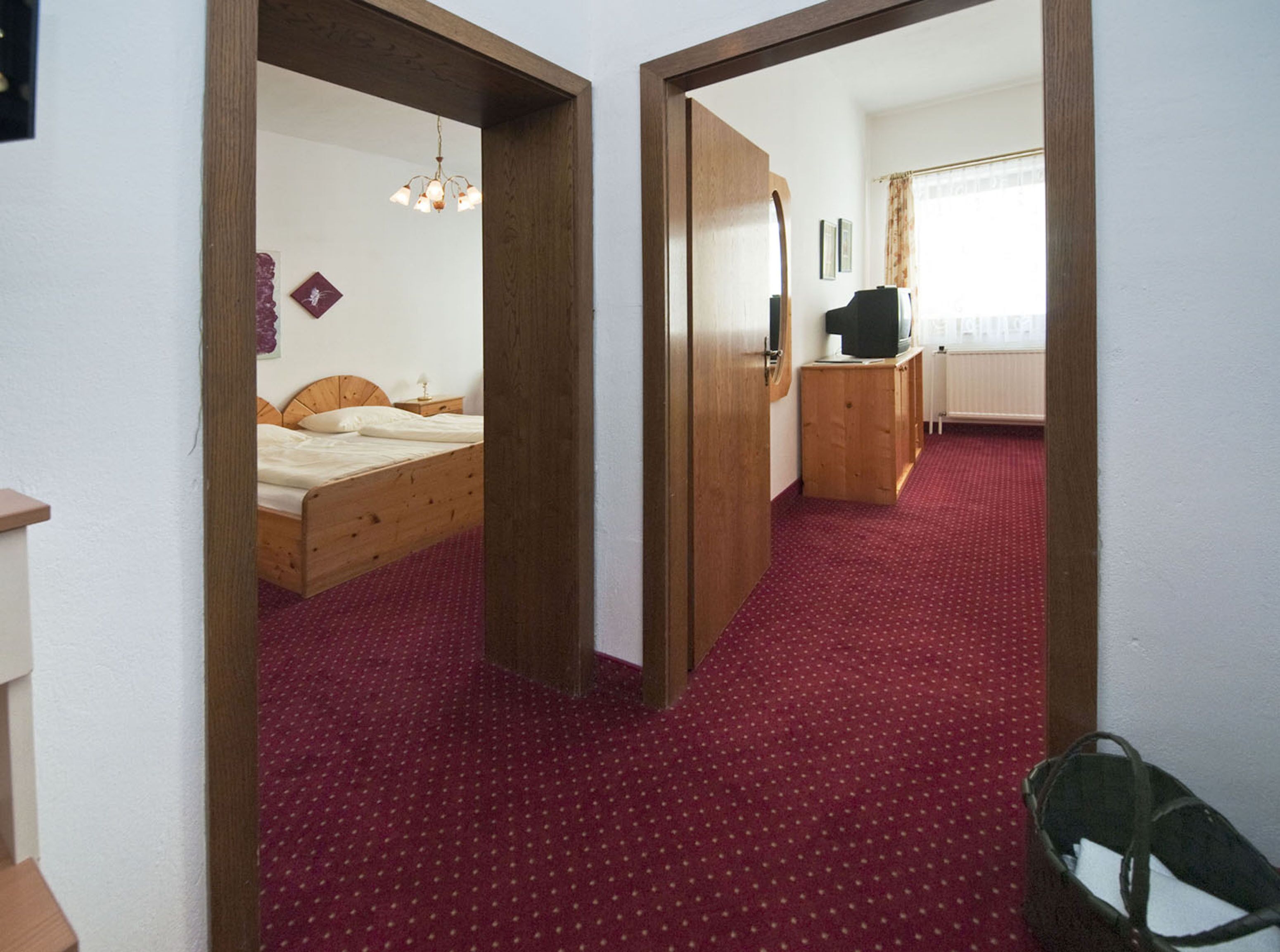 A bedroom with a wooden bed, a red carpet, and a wooden wardrobe.