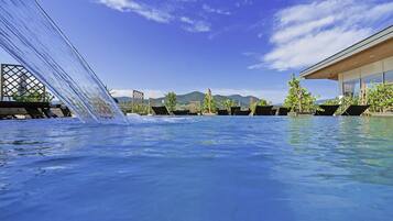 A pool with a waterfall feature, lounge chairs, and a view of mountains in the background.