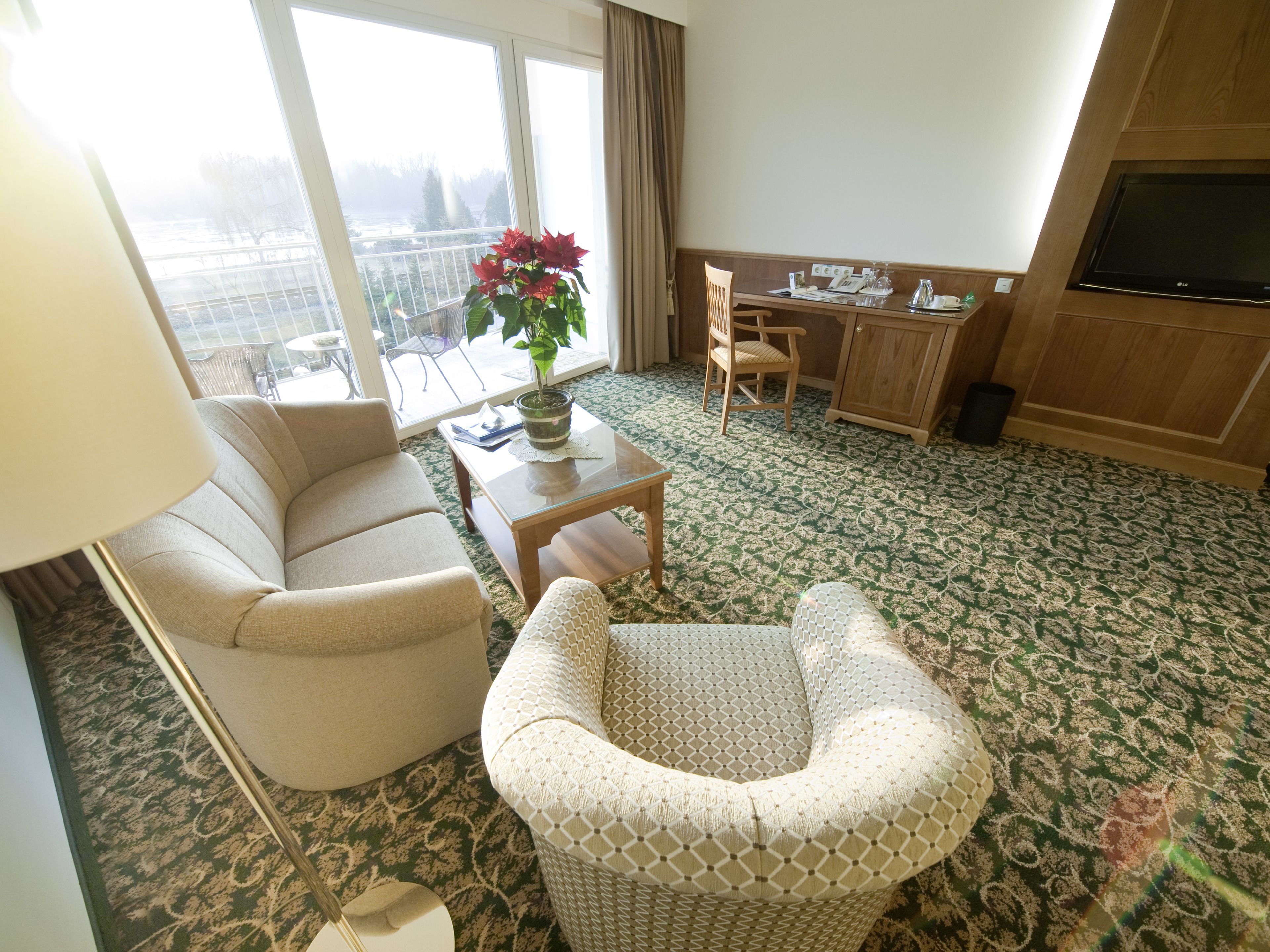 A hotel room with a sofa, armchair, dining table, and a TV.