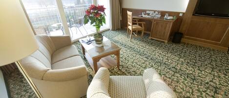A hotel room with a sofa, armchair, dining table, and a TV.