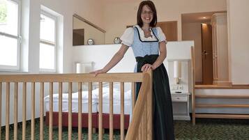 A hotel room with a wooden crib, a bed with white bedding, a mirror, and a nightstand with a lamp.