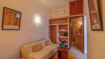 A cozy room with a striped sofa, a small wooden table with a vase, and a wardrobe with hanging clothes.