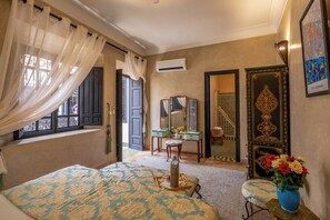 A bedroom with a bed, a vanity with a mirror, a chair, and a window with curtains. - Riad Saba (Marrakech)