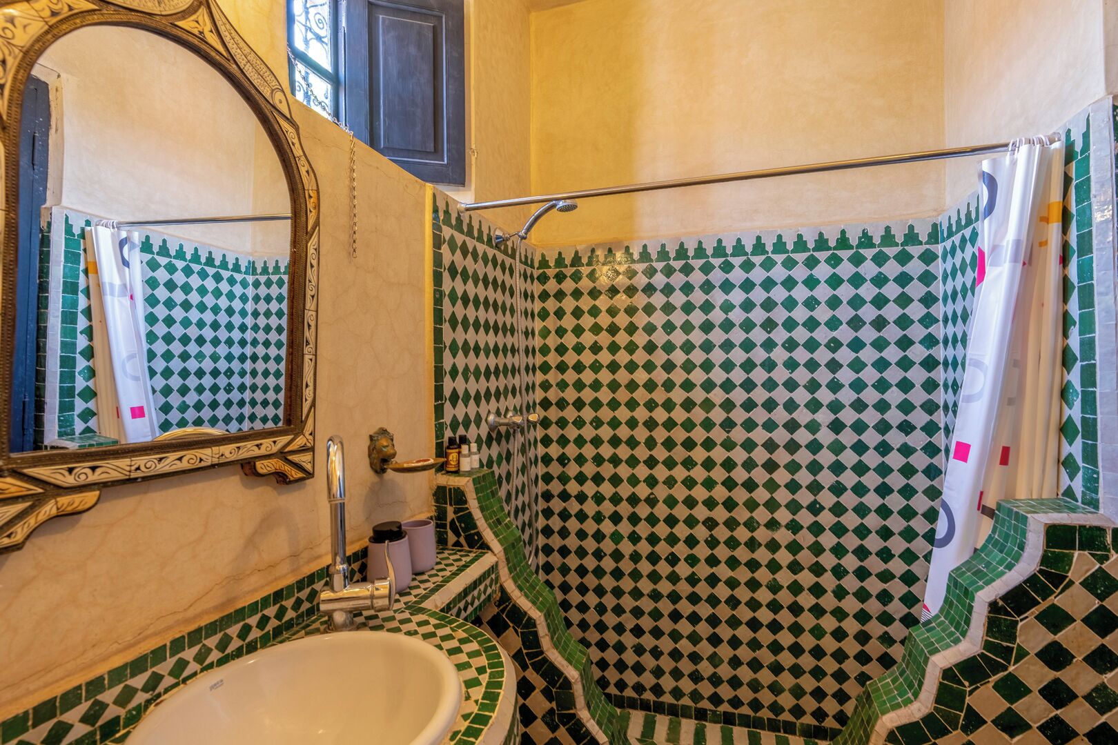 Un baño con lavamanos, espejo y ducha con baldosas blancas y verdes a cuadros.