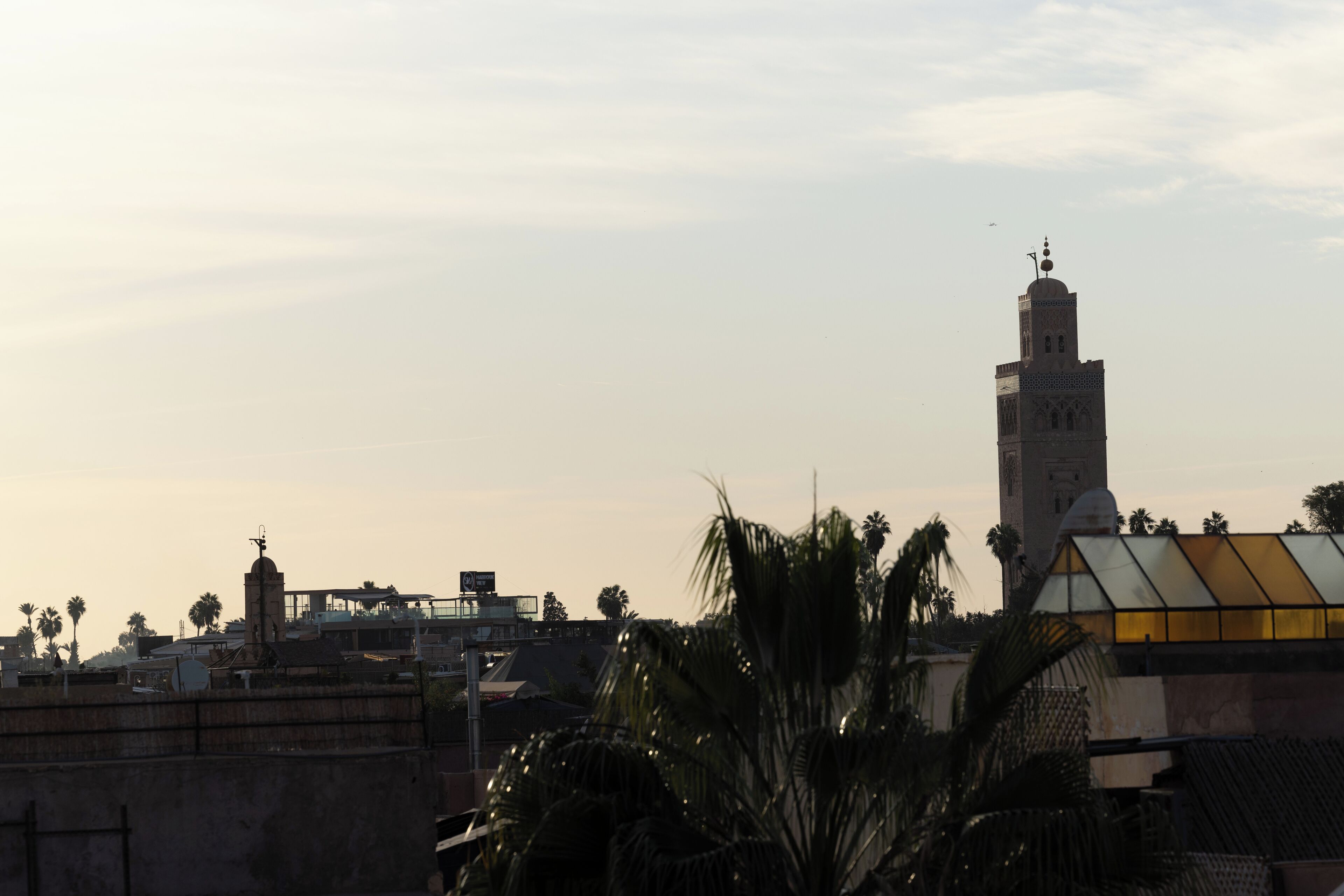 A tall tower with a minaret, surrounded by palm trees and buildings.