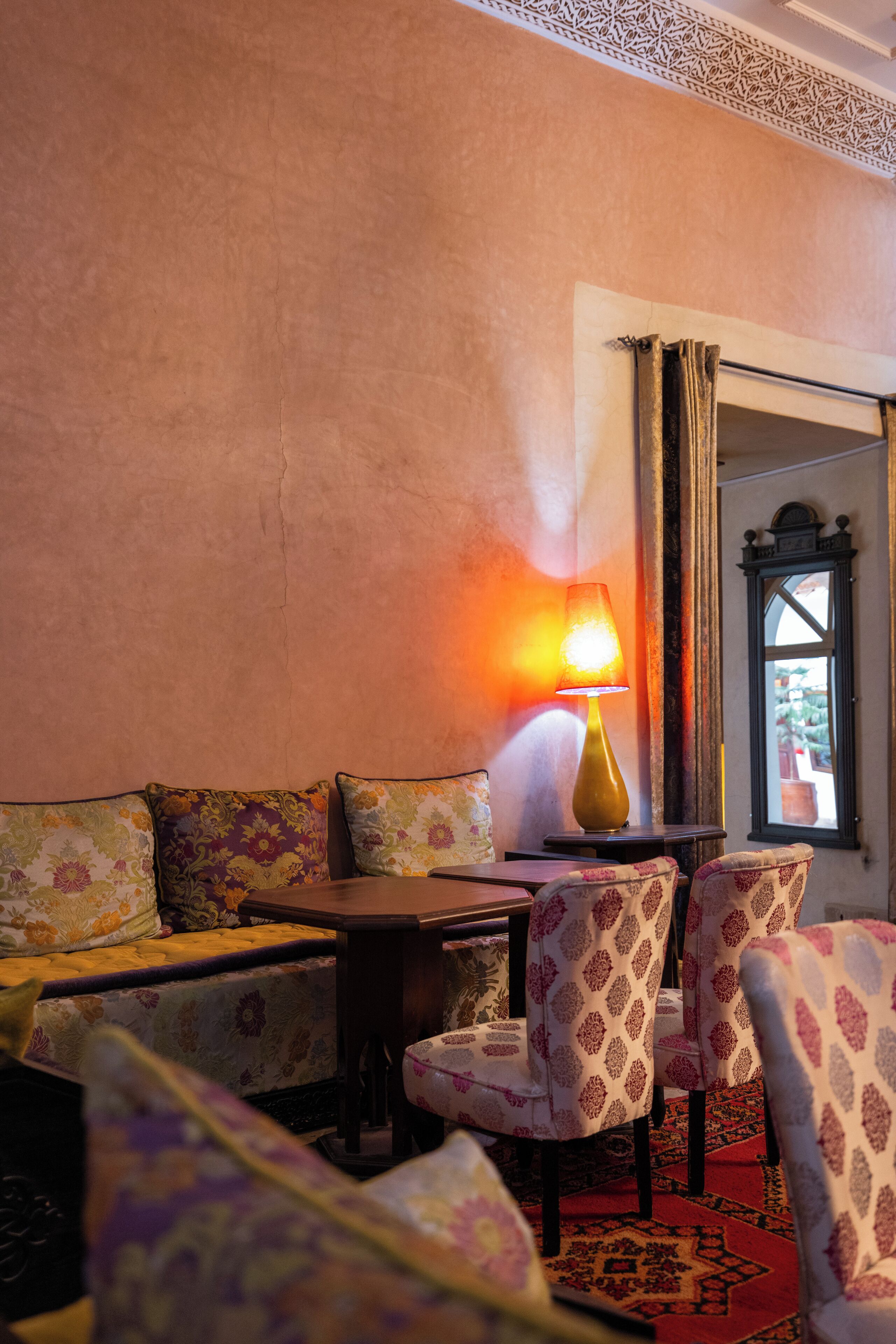 A cozy seating area with patterned cushions, a table with a lamp, and a view through a window.