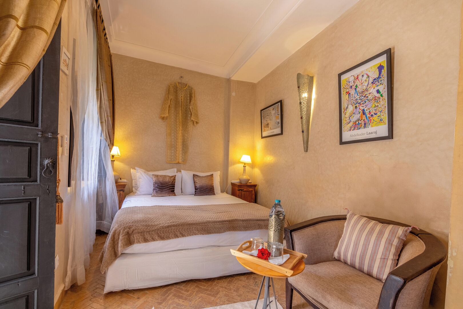 A hotel room with a bed, a sofa, a small table with a tray, and artwork on the walls.