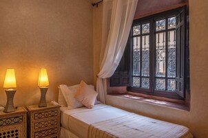 Una camera da letto accogliente e intima con un letto singolo, due lampade ai comodini e una finestra con ringhiere in ferro decorativo.