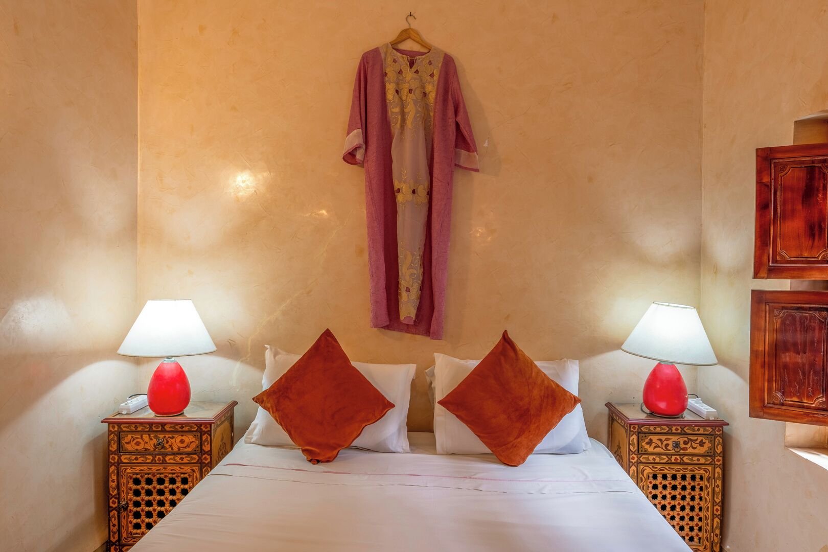 A hotel room with a bed, two nightstands with lamps, a hanging robe, and two decorative pillows.