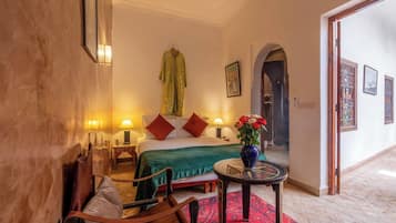 Una habitación de hotel con una cama, una silla, una mesita con un jarrón de flores y una alfombra roja.