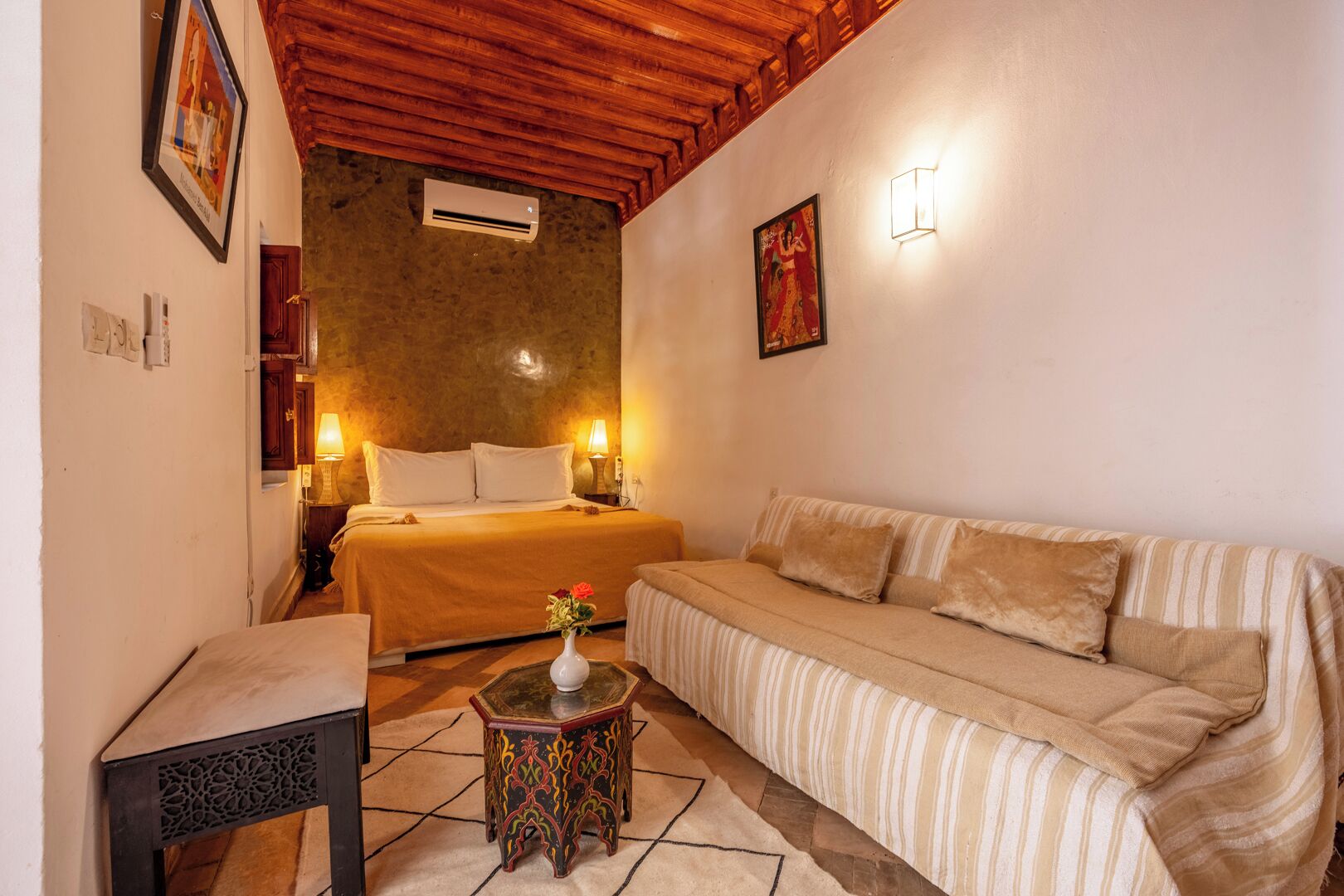 Une chambre d’hôtel confortable, avec un lit, un canapé, une petite table surmontée d’un vase et une applique murale décorative.