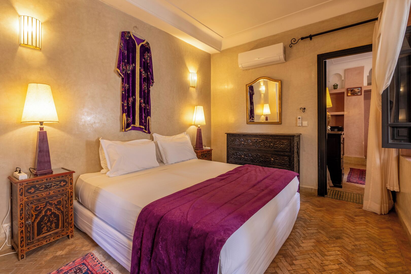 Habitación de hotel con una cama grande, dos lámparas de noche, un cabecero decorativo, un espejo y un equipo de aire acondicionado.