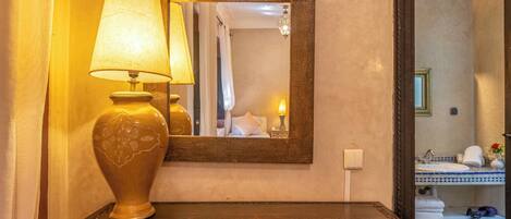 A wooden bedside table with a lamp and a mirror.