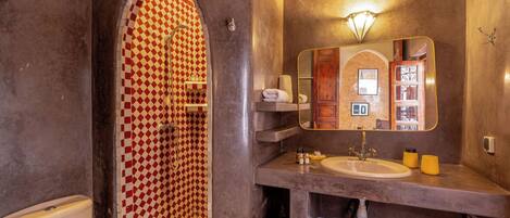 Un baño con pared de ducha a cuadros, un lavabo con espejo y un inodoro.