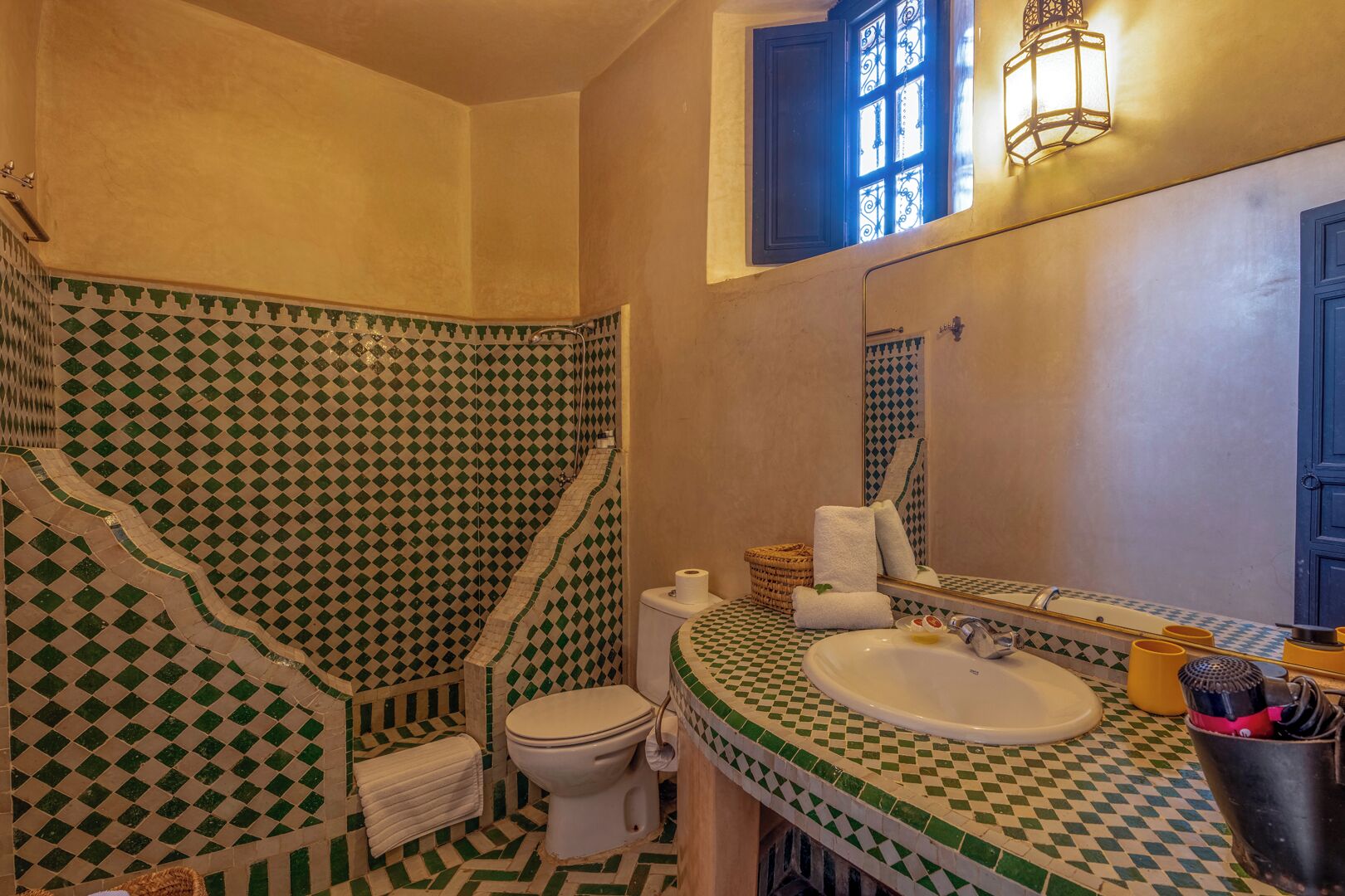 A bathroom with a checkered floor and walls, a white sink, a toilet, and a window with blue shutters.