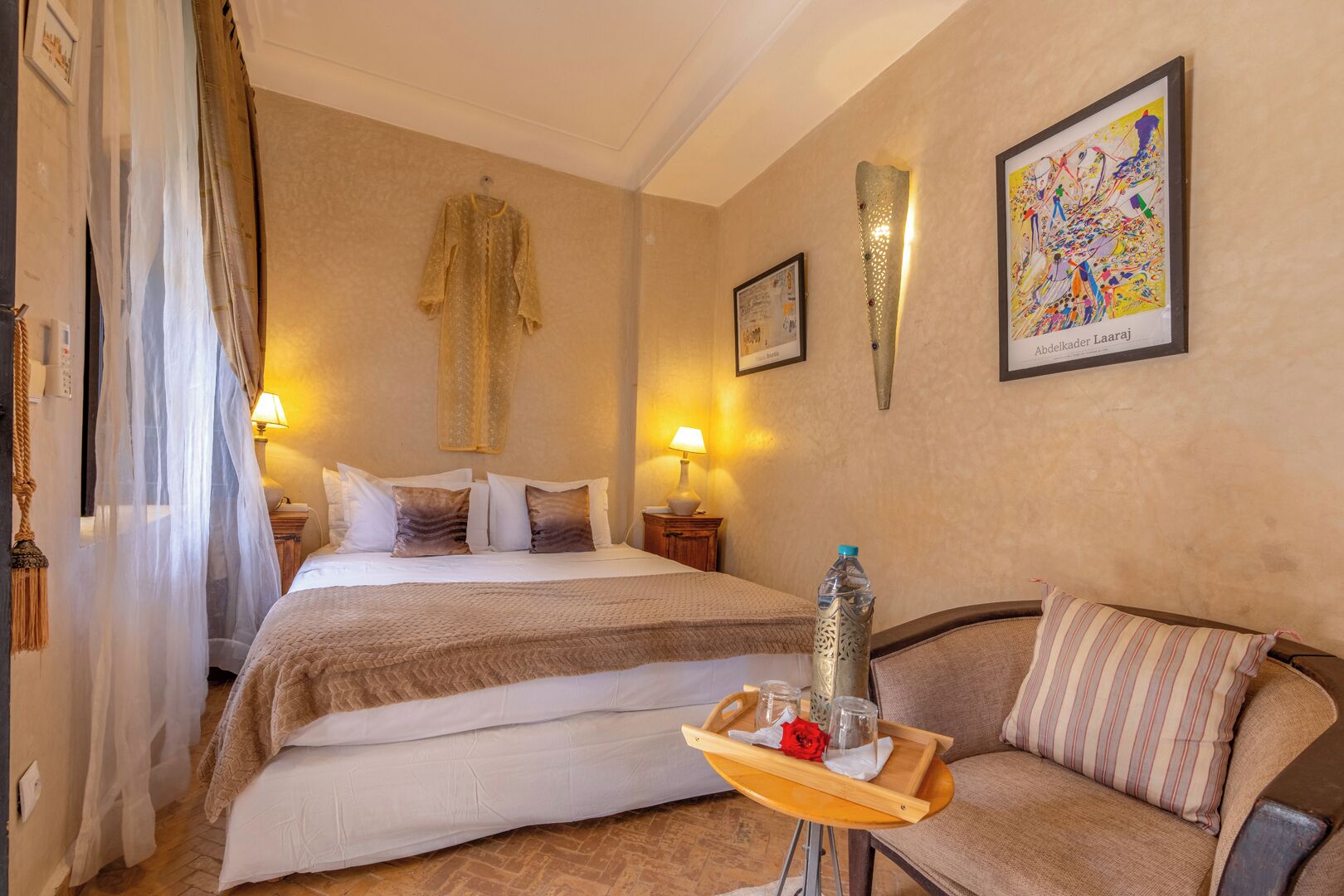 Habitació d'hotel amb un llit, un sofà, una bandeja amb gots i una ampolla, i un quadre a la paret.