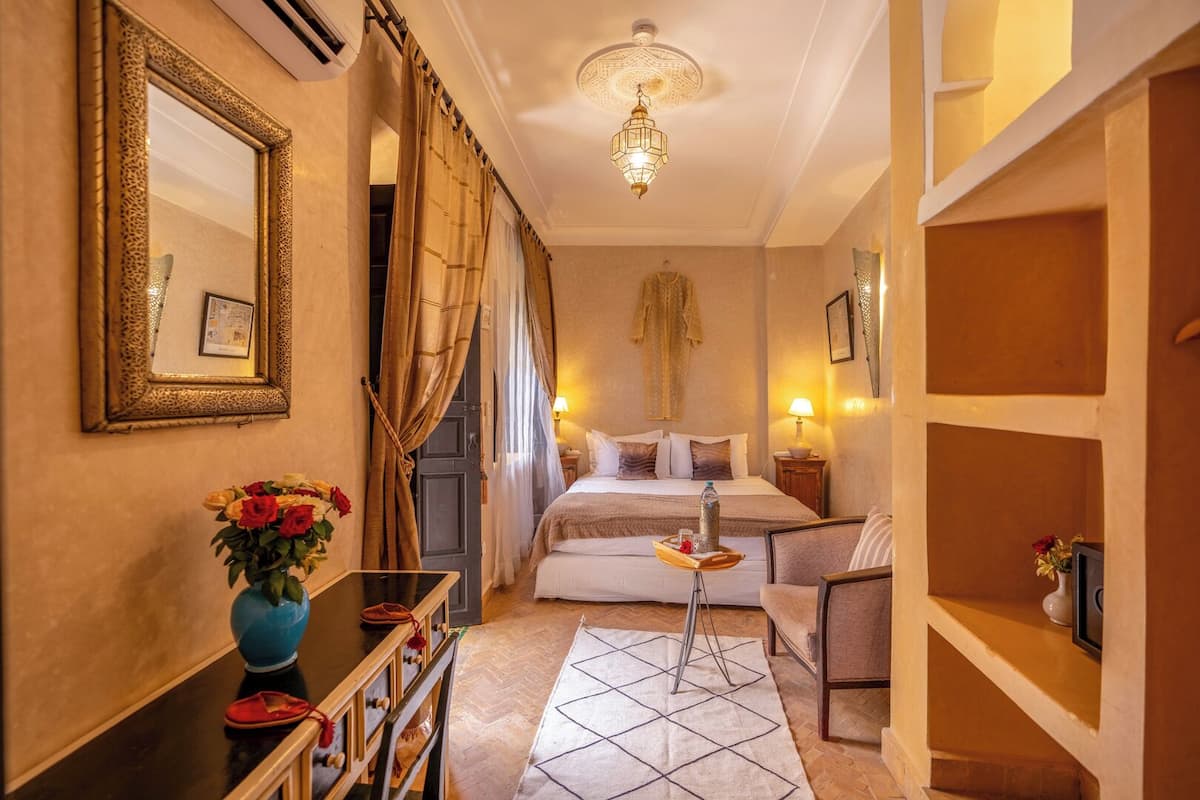 A hotel room with a bed, bedside table, chair, and a decorative mirror.