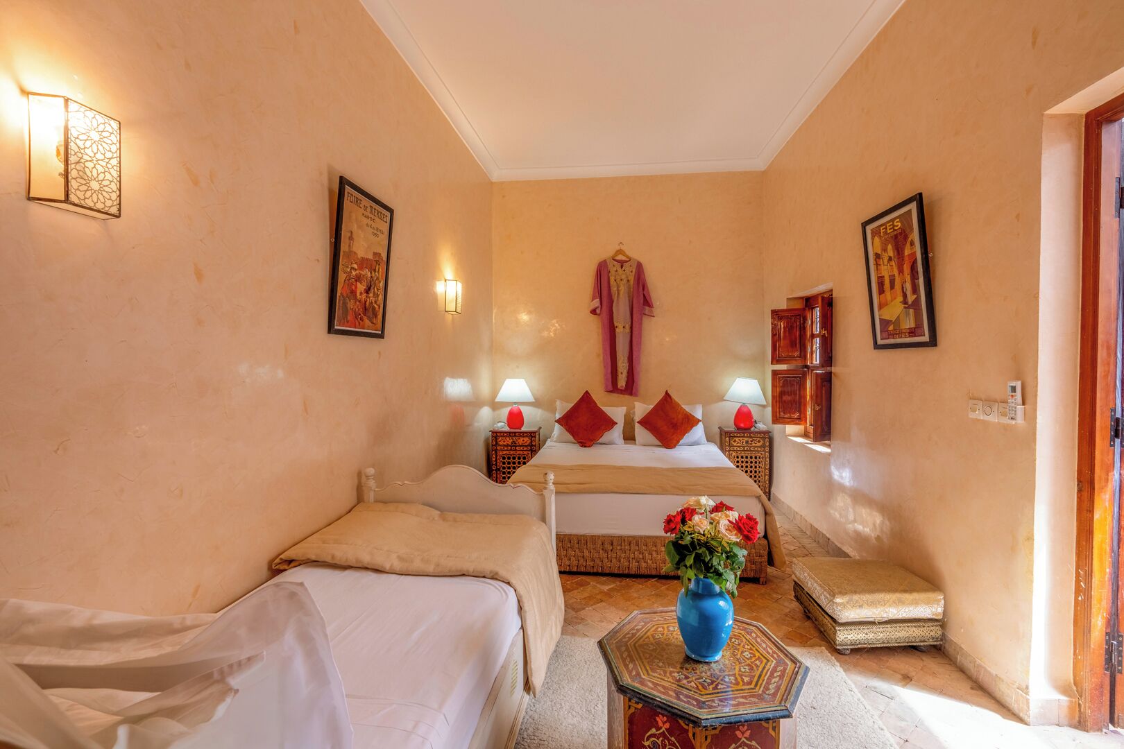 A hotel room with a bed, a sofa, a small table with a vase, and a door.