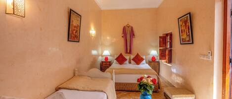A hotel room with a bed, a sofa, a small table with a vase, and a door.
