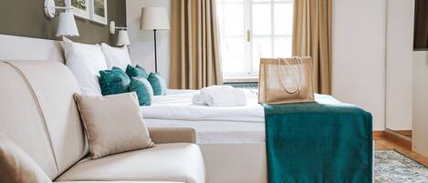 A hotel room with a bed, a sofa, a window with curtains, a lamp, and a bag on the bed.