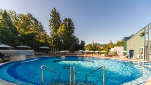 A swimming pool with a clear blue water, surrounded by lounge chairs and umbrellas, with trees and a building in the background. - Depandance Vila Higiea - Terme Dobrna (Dobrna)