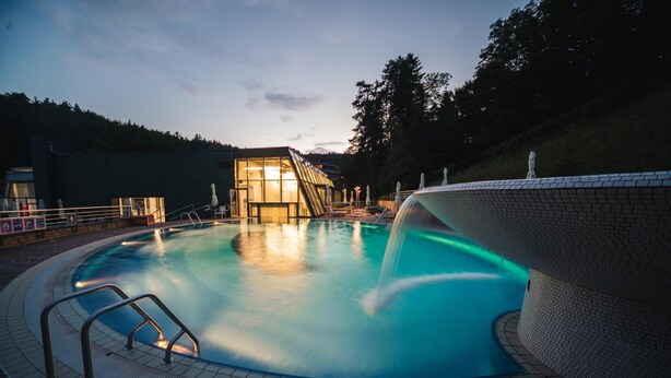 A swimming pool with a glass structure in the background, surrounded by a tiled deck and a fence. - Depandance Vila Higiea - Terme Dobrna (Dobrna)