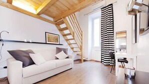 A modern living room with a white sofa, wooden flooring, a staircase, and a black and white striped curtain. - Maximus (Rome)