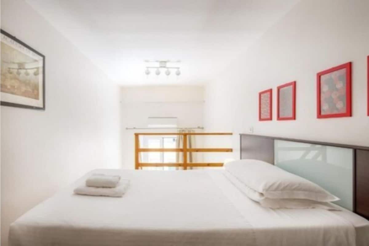 A hotel room with a bed, a bedside table, a window with a view, and a wall with framed pictures.