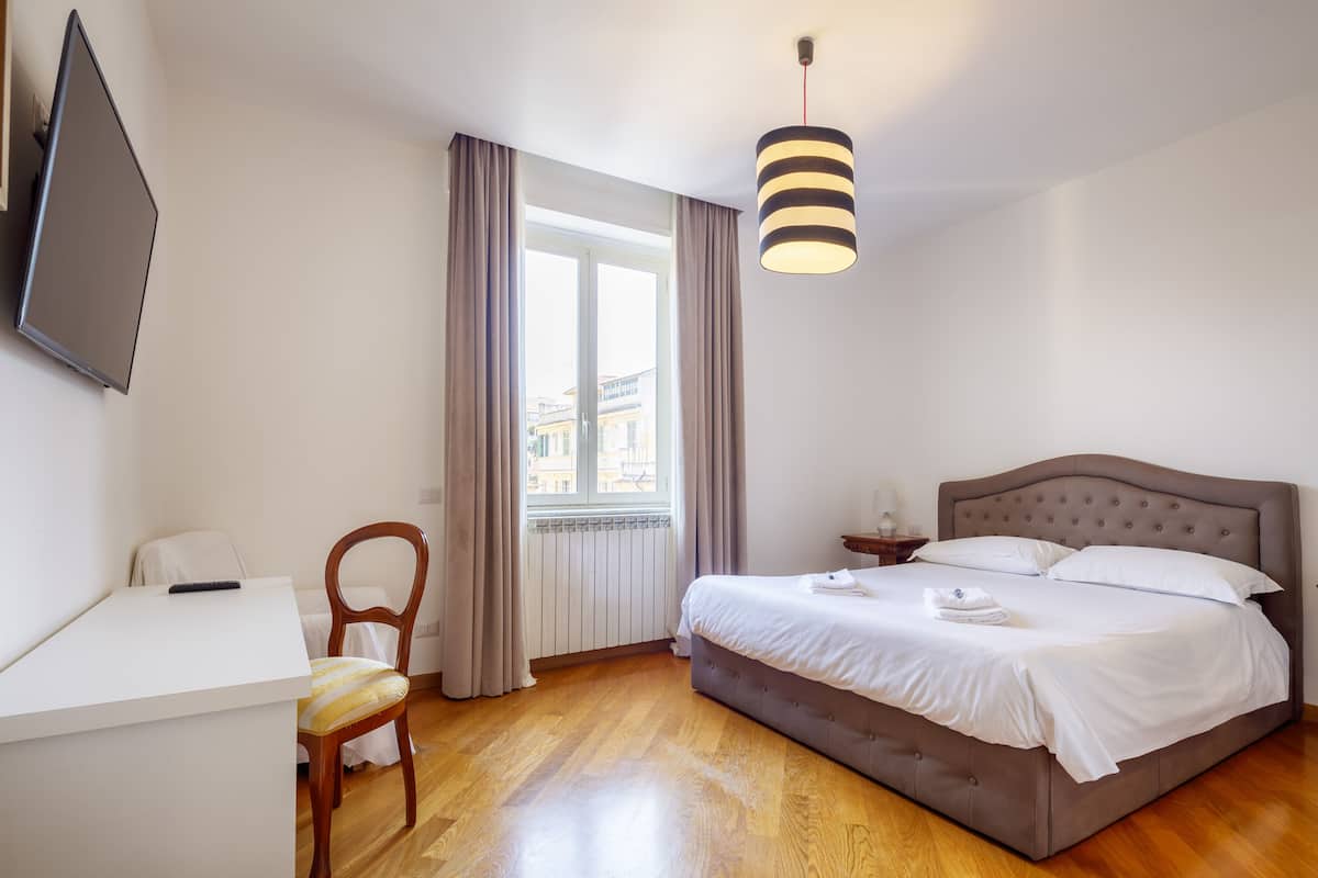 A hotel room with a bed, a desk, a chair, and a TV mounted on the wall.
