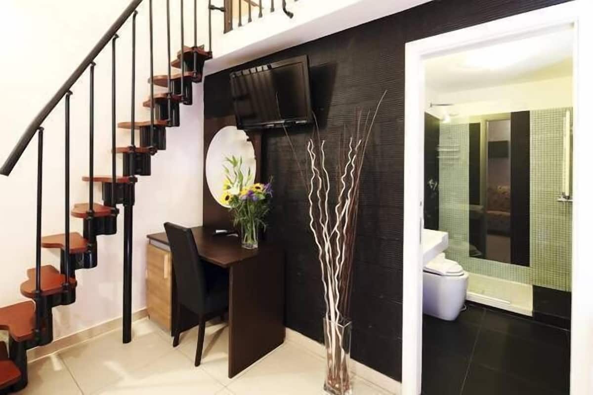 A modern interior with a staircase, a desk, a chair, a vase with flowers, and a bathroom visible through a glass door.
