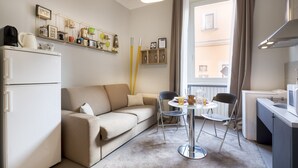 A compact living space with a kitchenette, a sofa, a dining table, and a window with curtains. - Maximus (Rome)