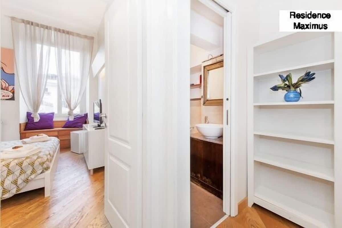 A bedroom with a bed, a window with curtains, a bedside table, and a wall-mounted TV.