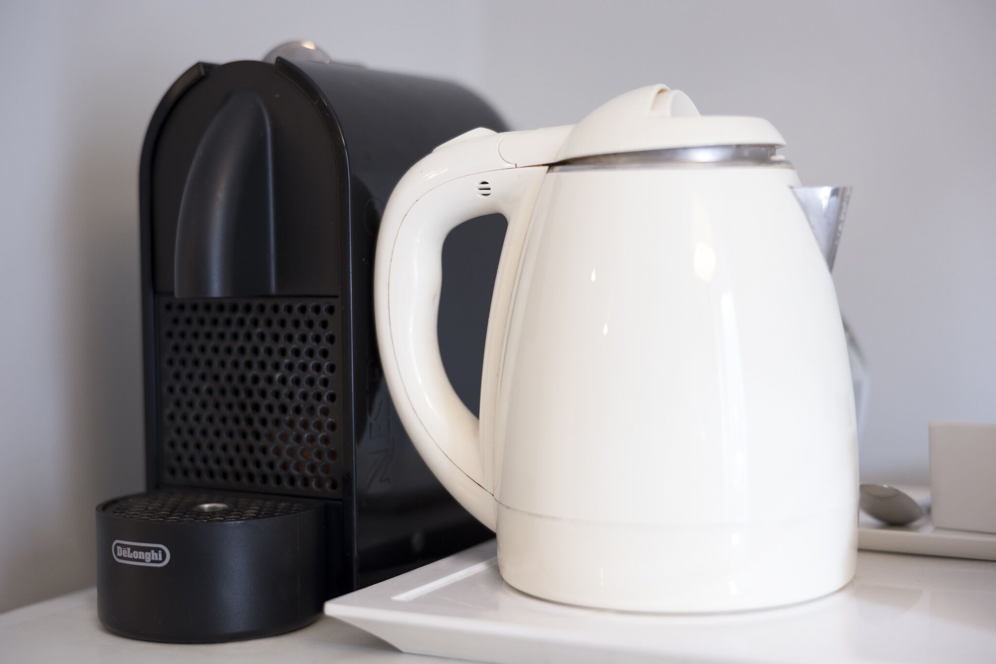 A black and white coffee maker and a white kettle on a white countertop.