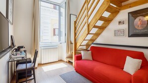 A room with a red sofa, a wooden staircase, a desk with a chair, and a window with curtains. - Maximus (Rome)