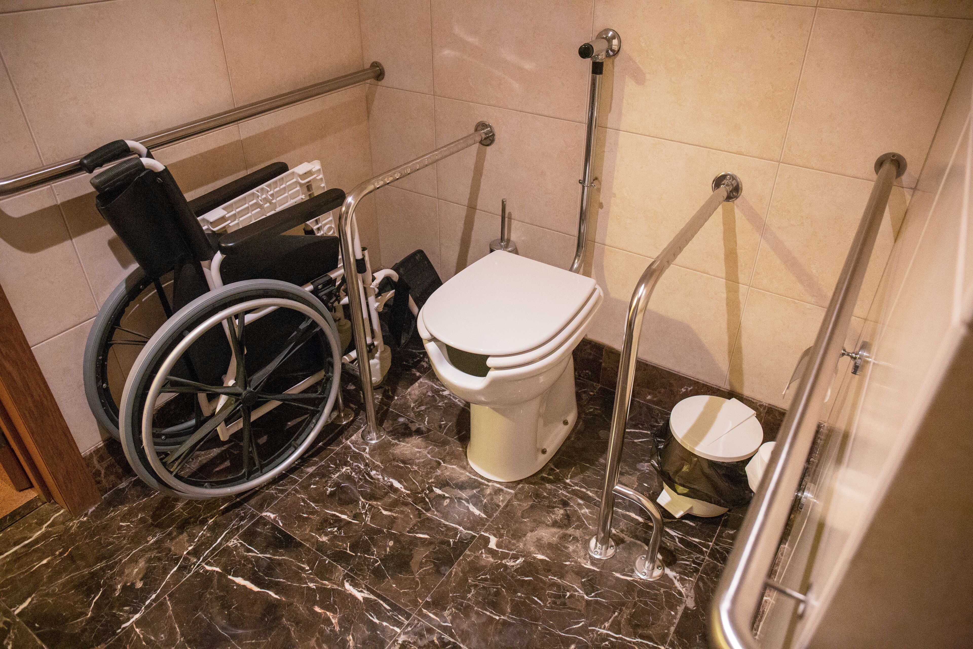A wheelchair-accessible bathroom with a toilet, grab bars, and a wheelchair.