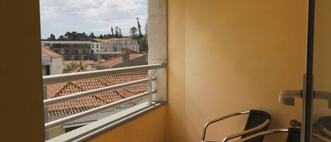 Balcón con vista a edificios y un tejado de tejas. Hay dos sillas y una puerta.