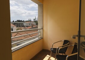 A balcony with a view of buildings and a tiled roof. There are two chairs and a door.