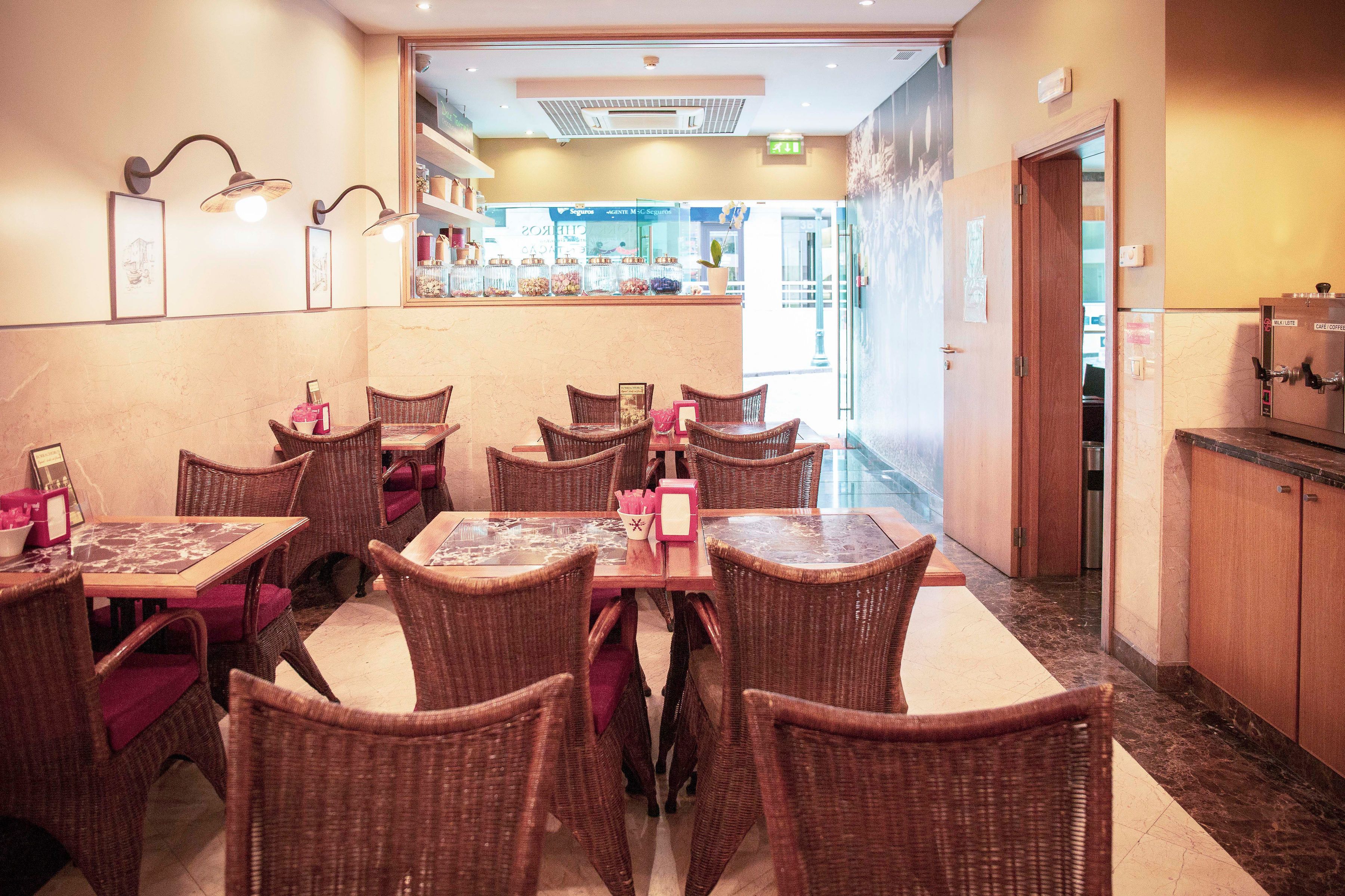 A restaurant with wicker furniture, a counter with a display of items, and a door leading to another area.