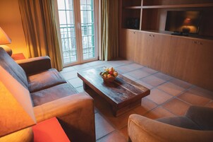 A living room with a sofa, a coffee table with a fruit basket, and a television on a wooden cabinet.