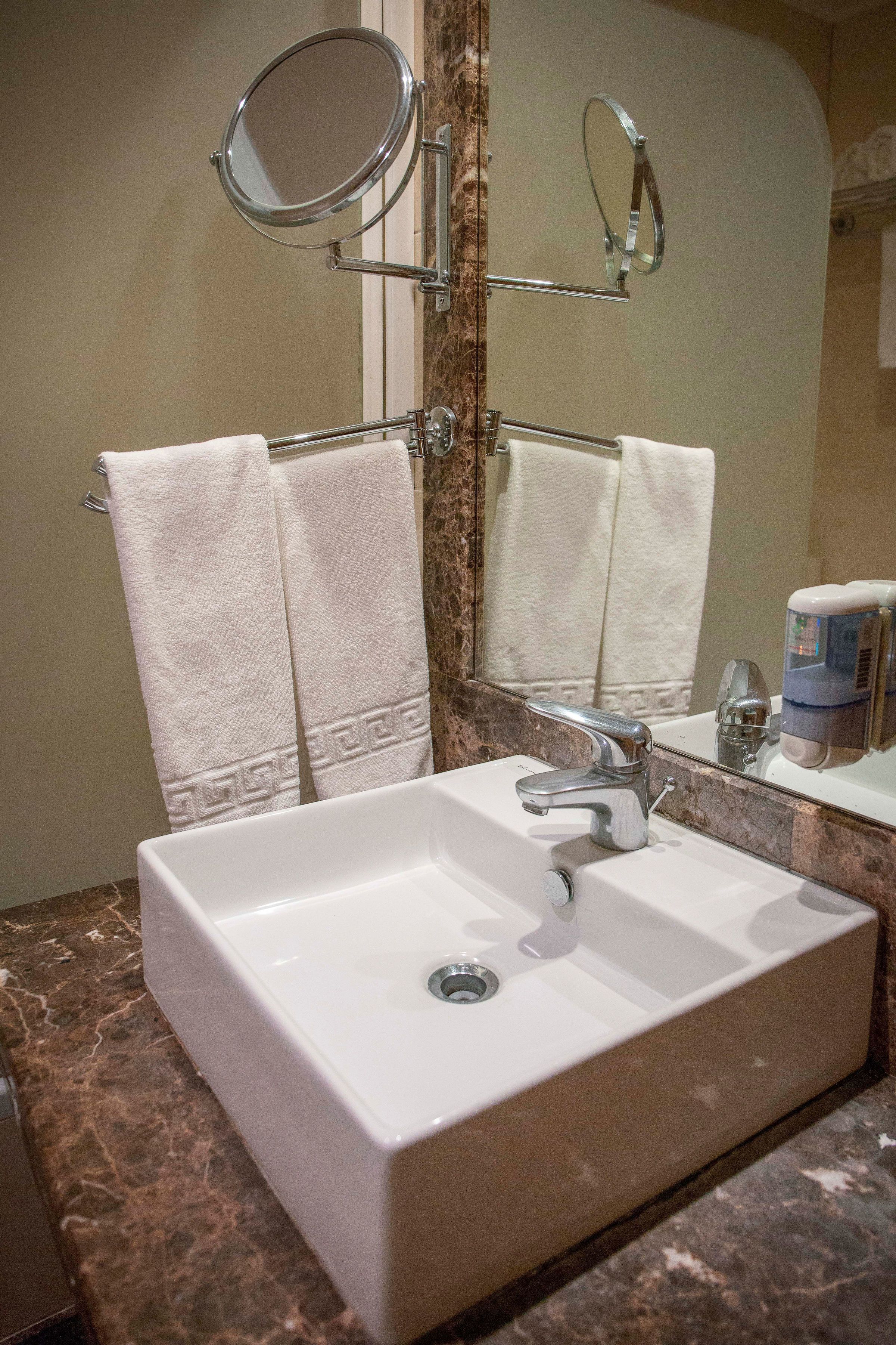 Une salle de bain avec un lavabo blanc, un miroir et deux serviettes suspendues à un porte-serviettes.