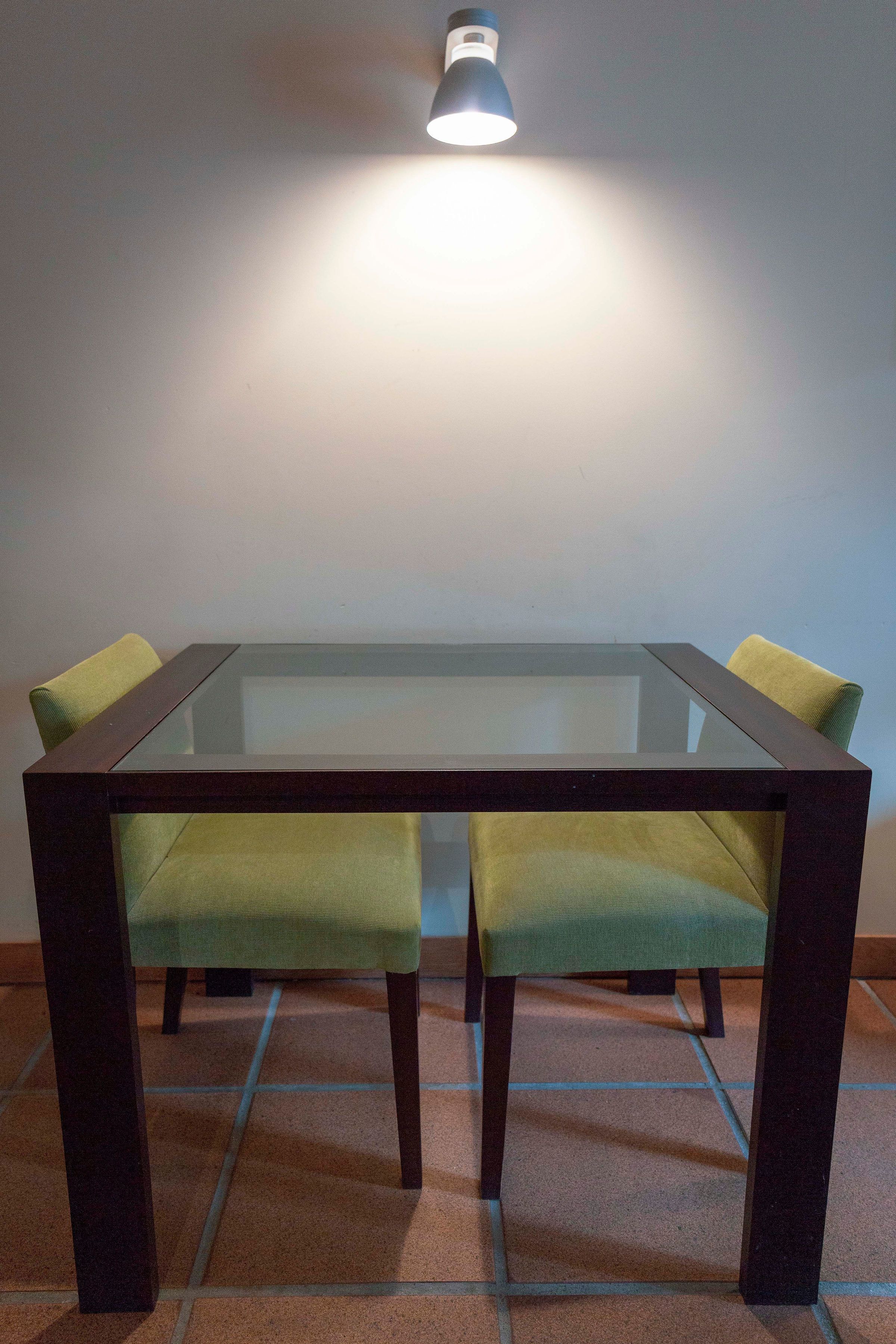 A glass-top dining table with two chairs, each with a green cushion.