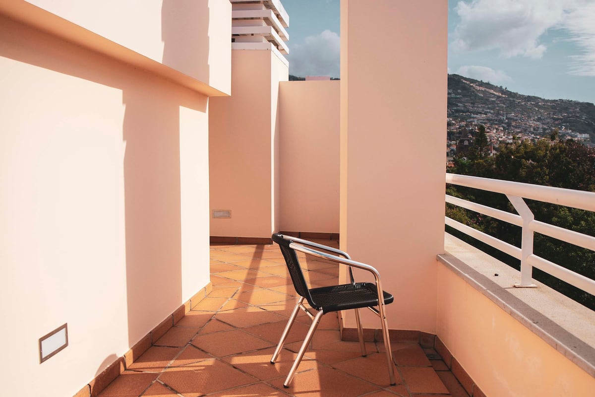 A balcony with a chair, white walls, and a view of a town.