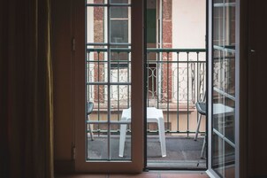 A view through a glass door to an outdoor balcony with a white chair and a metal railing.