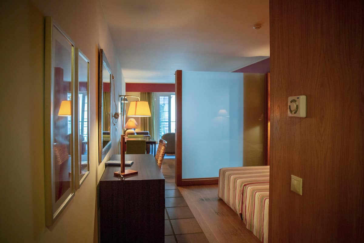 A hotel hallway with a wooden desk, a bed with striped bedding, and a door with a light switch.
