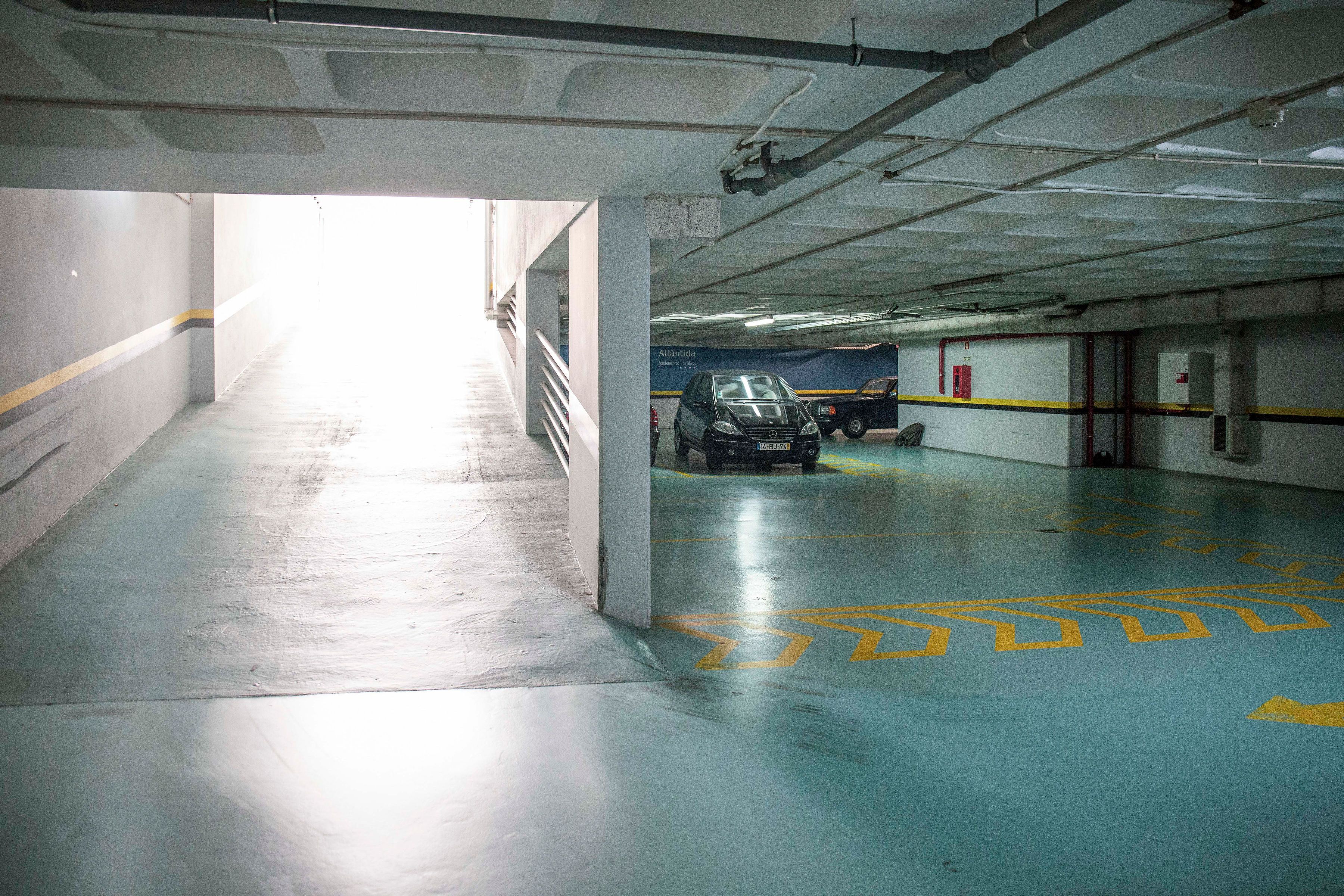 An underground parking garage with a car parked in the distance, concrete walls, and a blue floor with yellow markings.