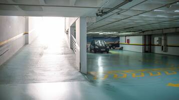 An underground parking garage with a car parked in the distance, concrete walls, and a blue floor with yellow markings.