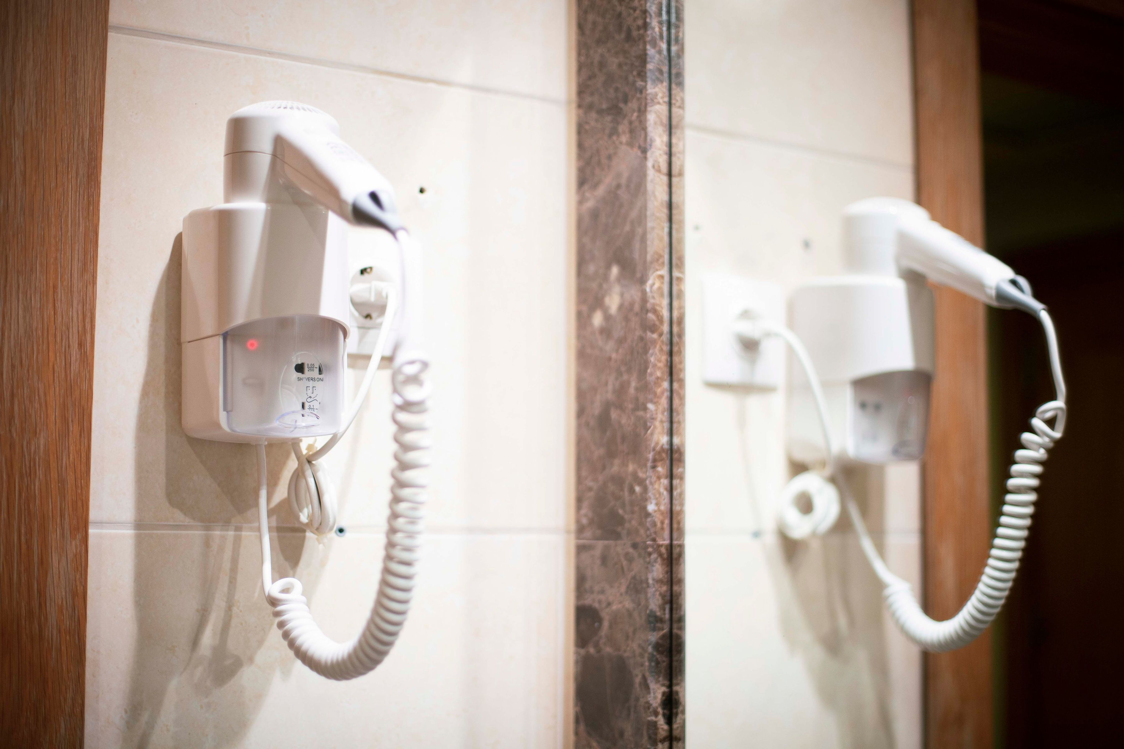 Een badkamer met twee haardrogers aan de muur, een marmeren kolom en een houten deur.