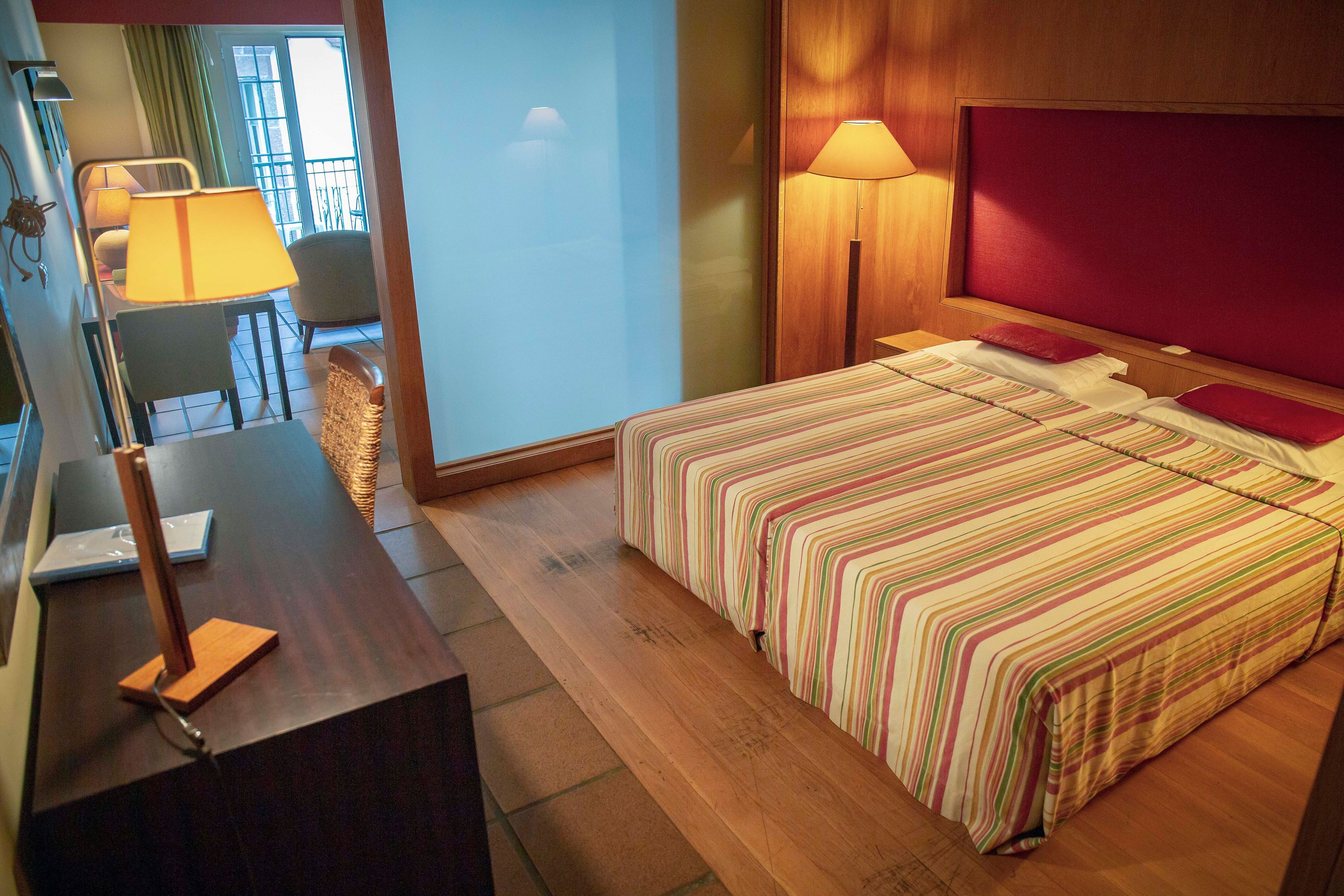 Een hotelkamer met een bed, bedlampjes, een bureau met een lamp en uitzicht op het balkon.